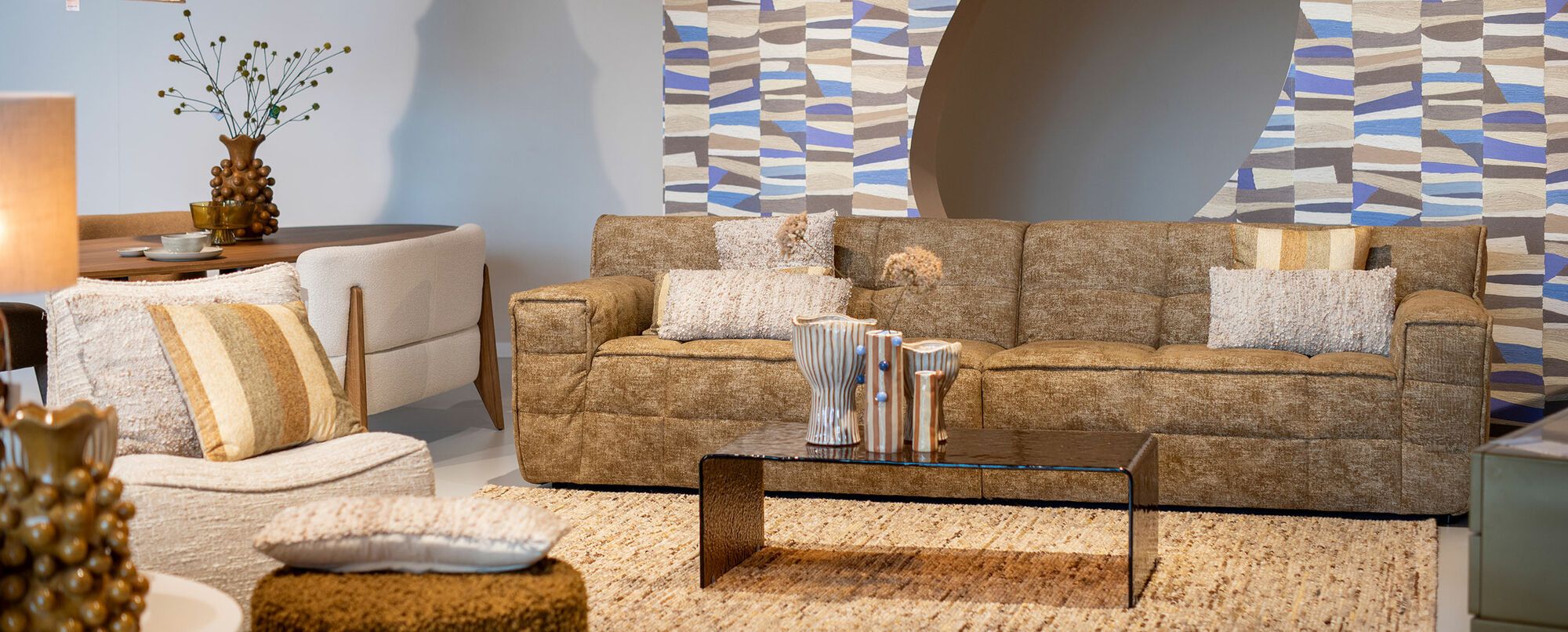 Grote beige hoekbank met blauwe kussens en houten salontafels op rond vloerkleed