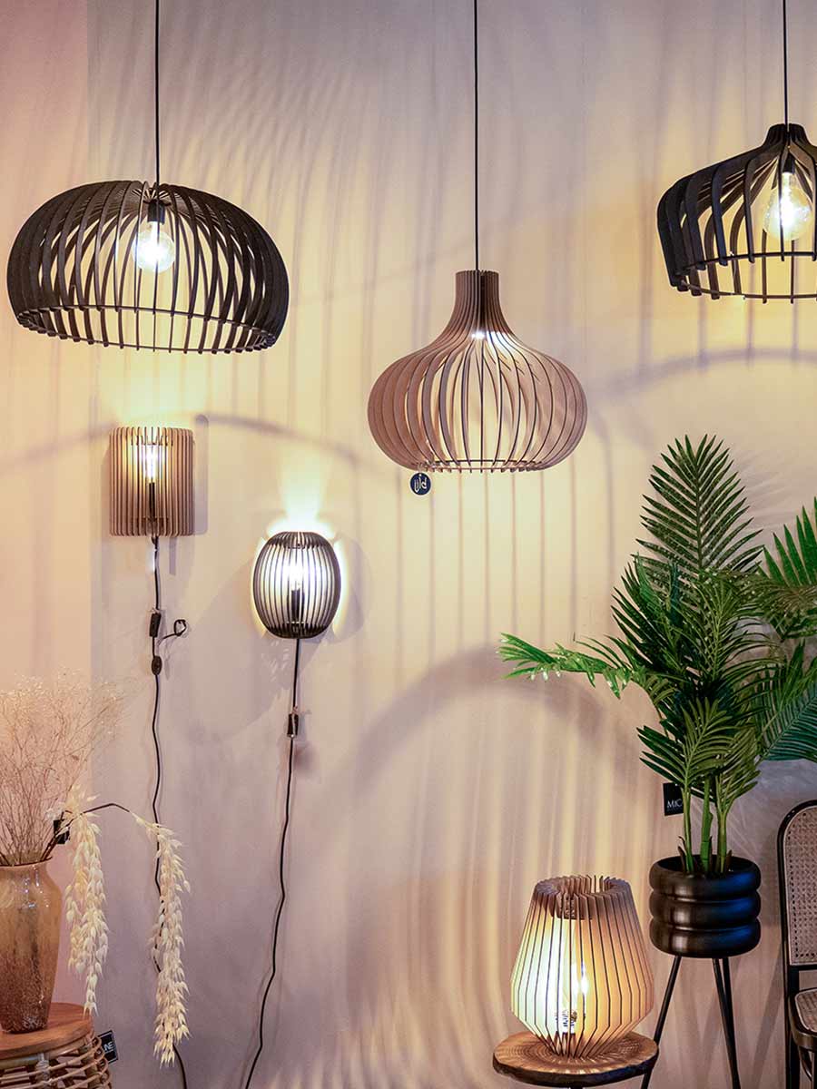 Combinatie van hanglampen, wandlampen en tafellampen van hout met opengewerkte structuren, die warme schaduwen creëren tegen een lichtgekleurde muur.