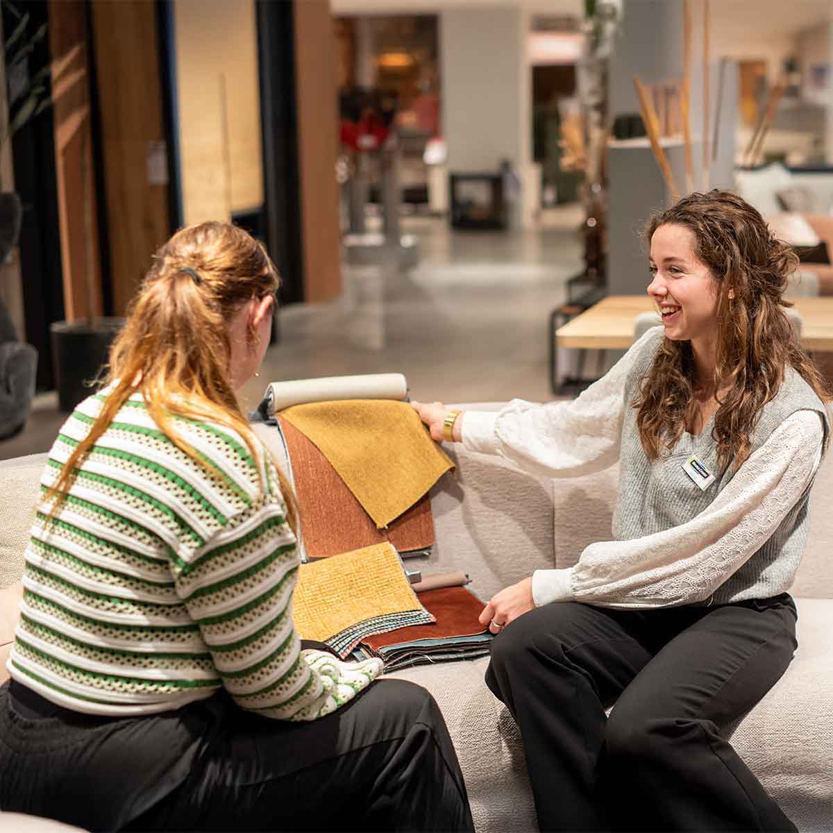 Een verkoopster laat stoffen zien aan een klant in een meubelwinkel