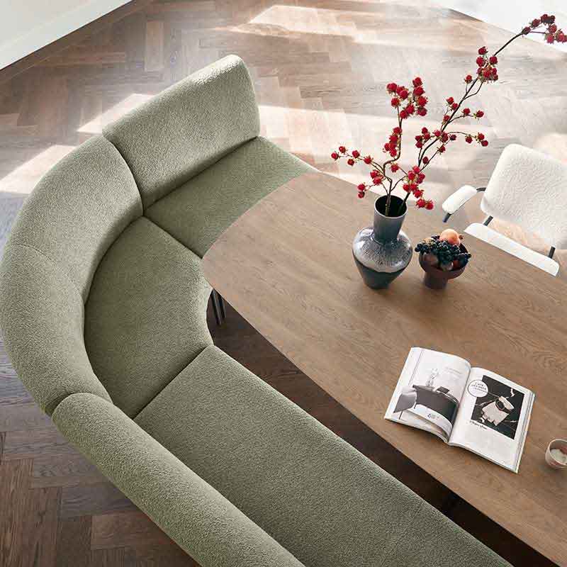 Een zithoek van boven met een houten eettafel en een groene zitbank