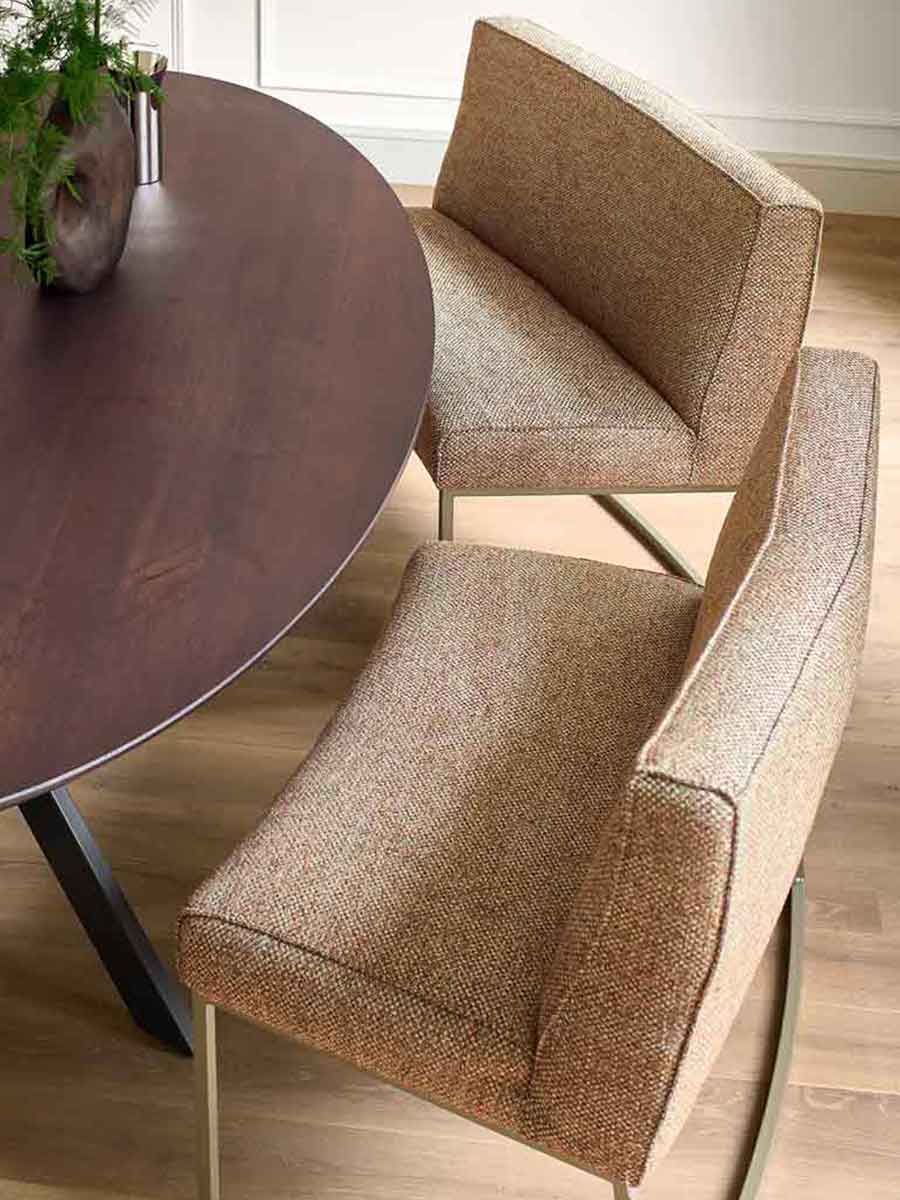 Twee moderne eetkamerbanken met hoge rugleuning en textiele bekleding in warme bruintinten, geplaatst aan een donkere ovale tafel op een houten vloer.