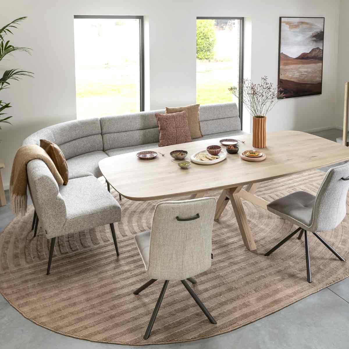 Een zithoek met een ronde eetbank en twee losse eetkamerstoelen in beige tinten