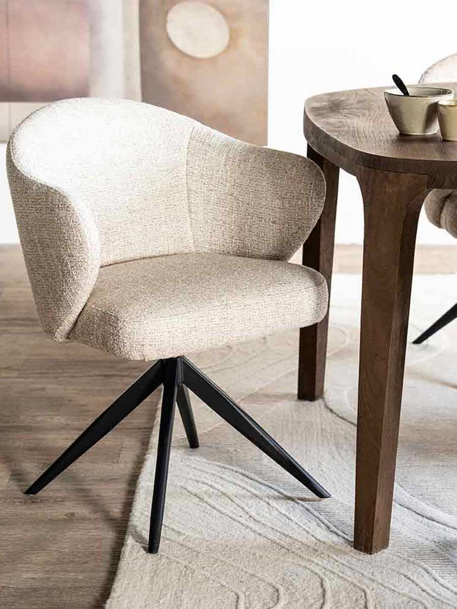 Comfortabele eetkamerstoel met ronde rugleuning in licht gemêleerde stof, op zwarte metalen draaipoot, geplaatst aan een houten eettafel op een zacht vloerkleed.