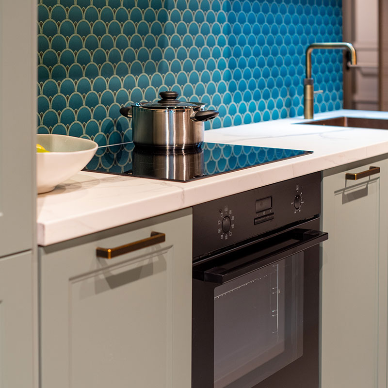 Groene keuken met wit werkblad, blauwe tegelwand en zwarte oven