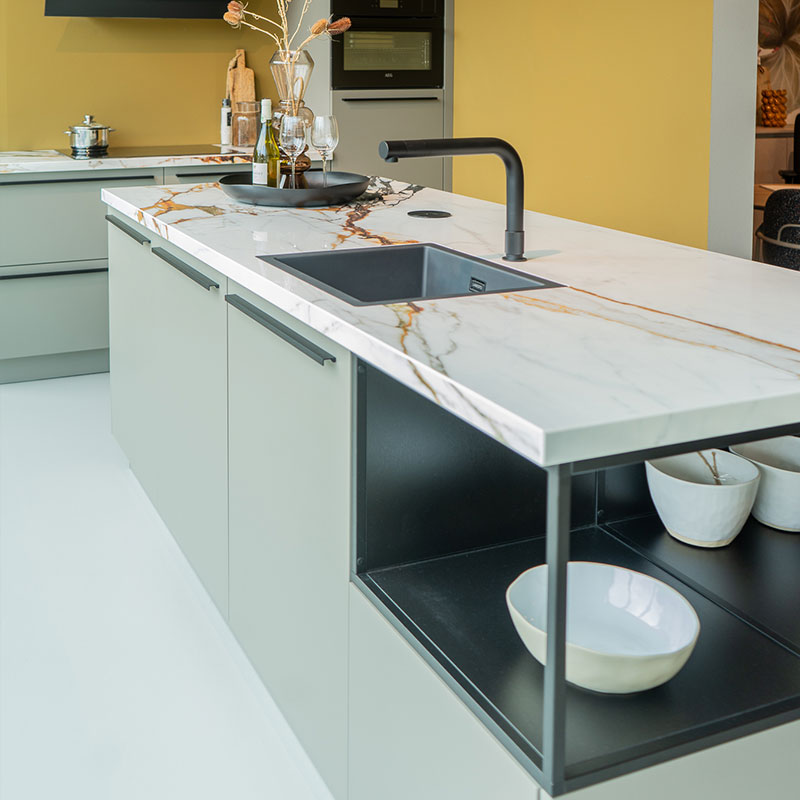 Groene keuken met marmeren werkblad, zwarte kraan en open vakken met witte schalen