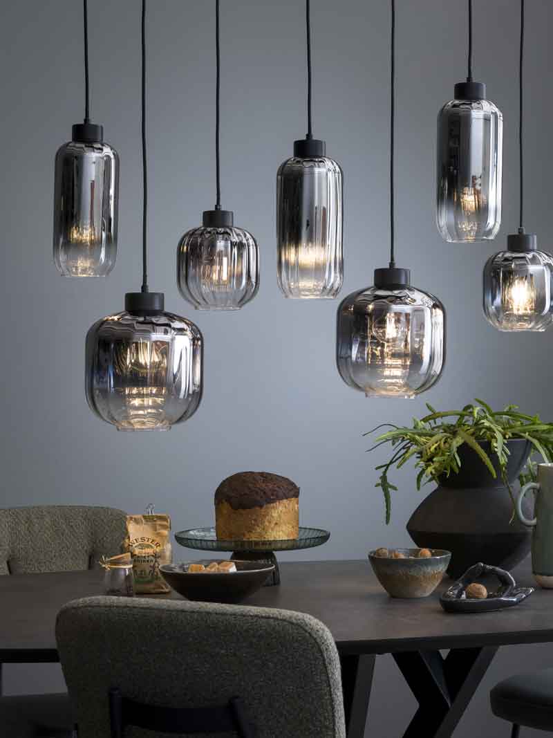 Zeven kleine hanglampen van donker glas boven een donkere eettafel 