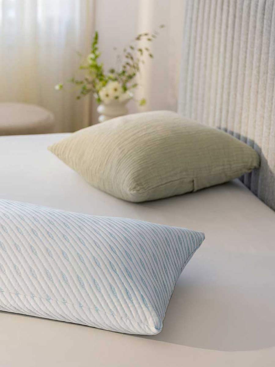 Twee ergonomische hoofdkussens in zachte hoezen, gepositioneerd op een strak opgemaakt bed in een lichte en rustgevende slaapkamer.