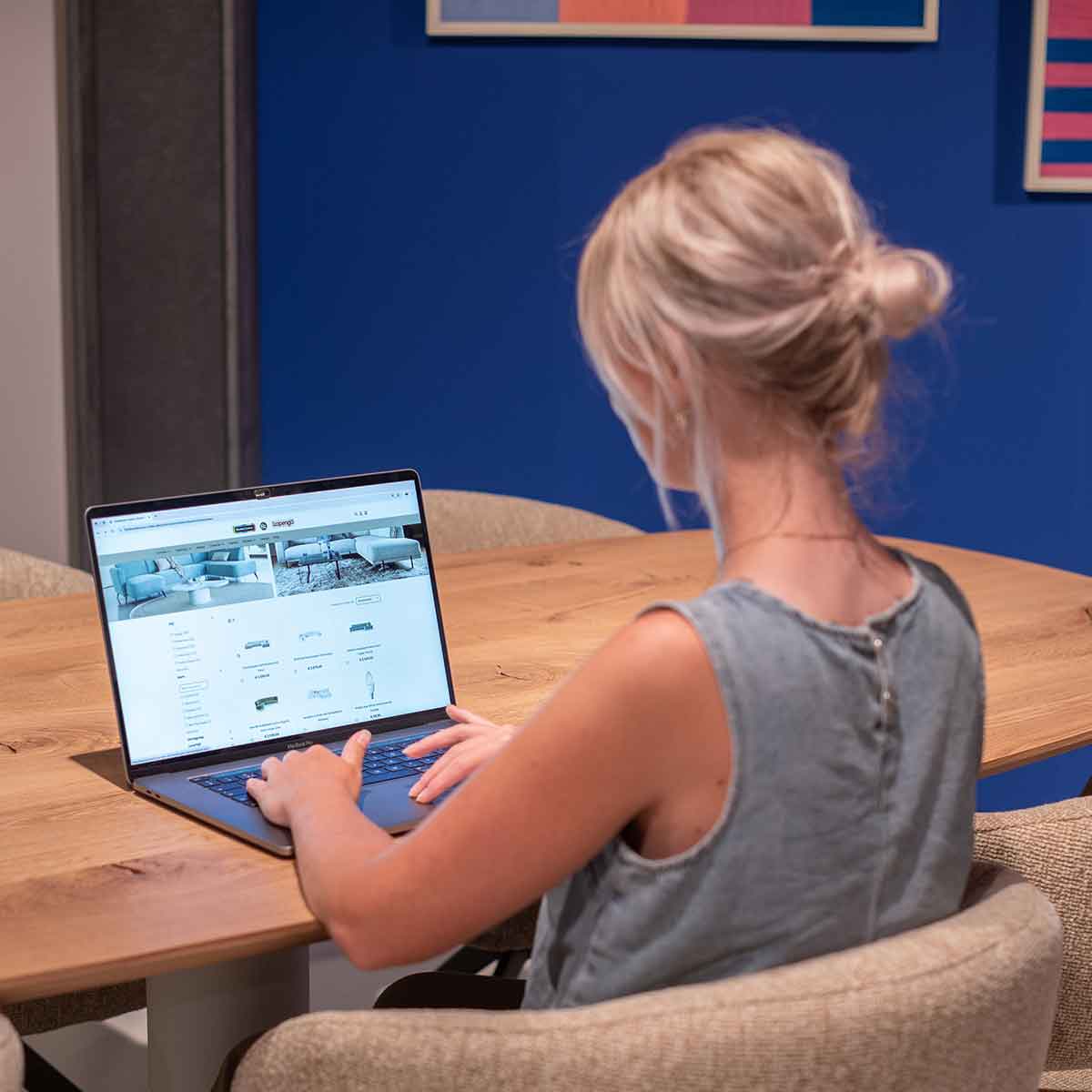 Blonde vrouw zit voor laptop en bekijkt een webpagina met meubelen