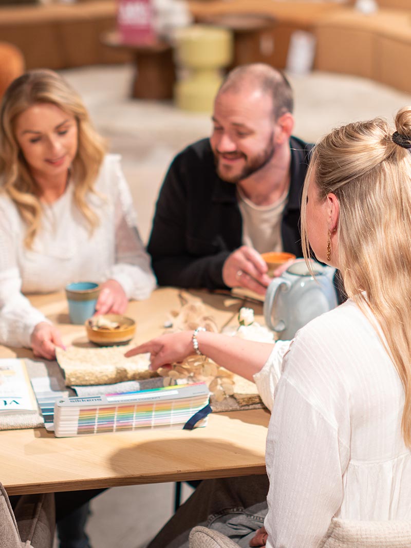 Vrouw wijst naar woonstalen en geeft interieuradvies aan een koppel