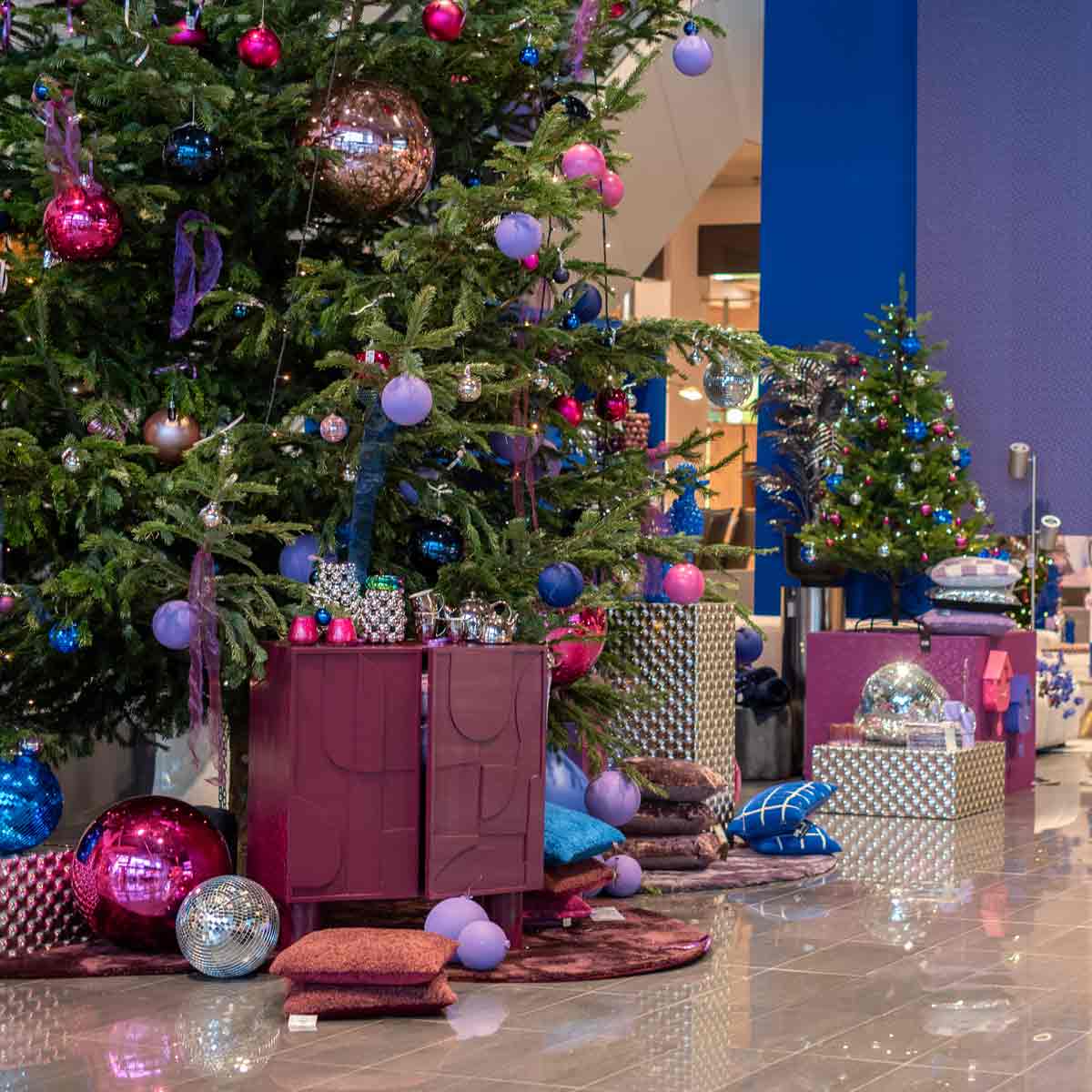 Een kerstboom in de hal van Home Center met paarse en roze kerstballen