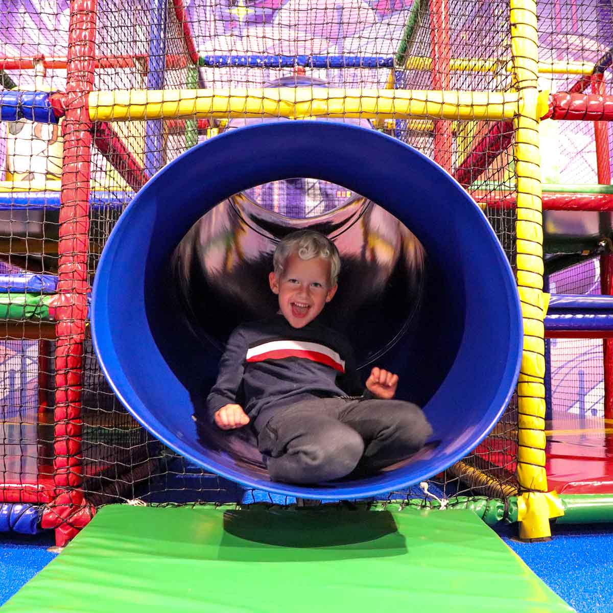 Een blij kind in een blauwe glijbaan in het kinderdorp van Home Center