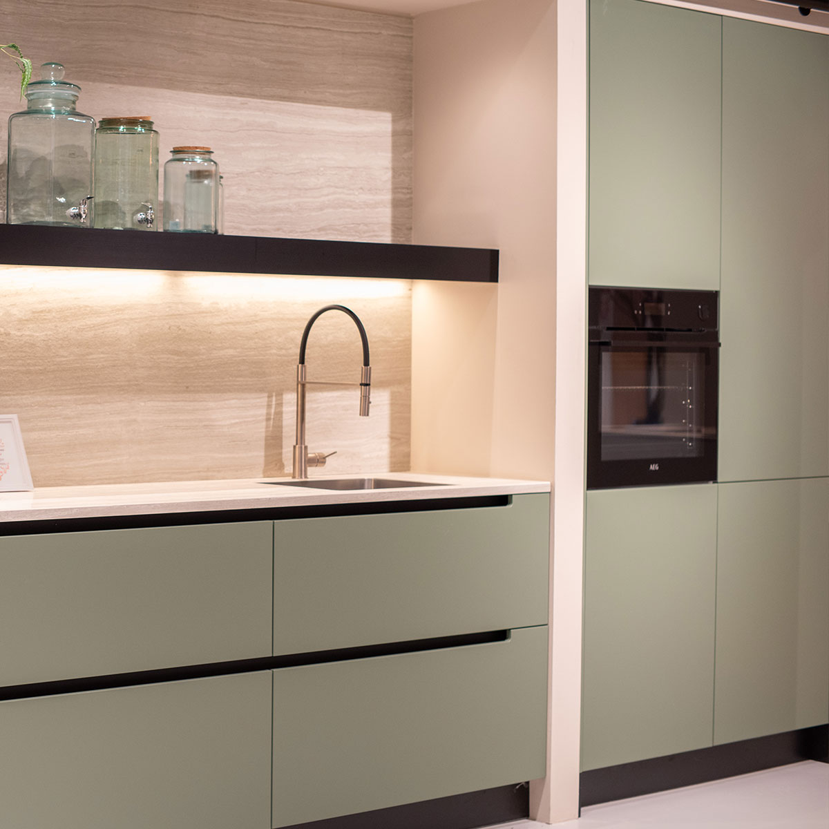 Moderne mintgroene keuken met zwarte oven, marmeren achterwand en ingebouwde spoelbak.