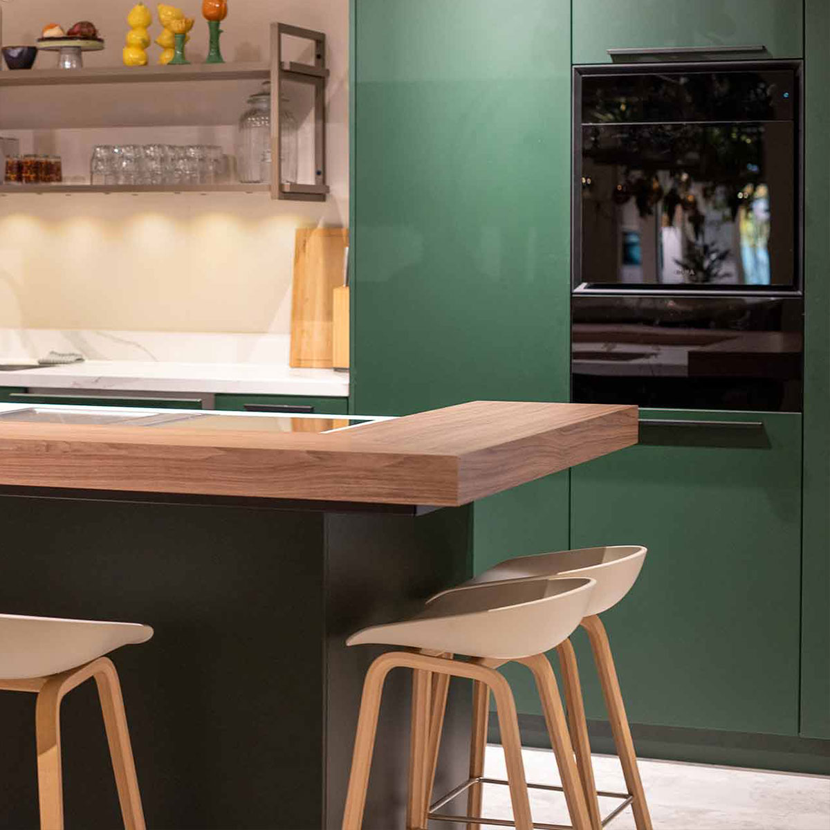 Mosgroene keukenwand met zwart inbouwoven en houten kookeiland met barkrukken