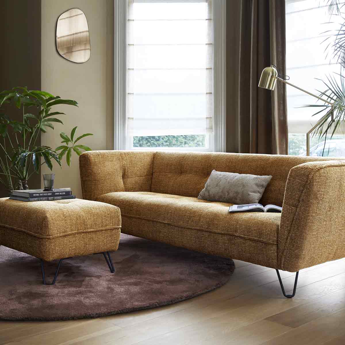 Een geelbruine rechte bank met rechte vormen en bijpassende hocker