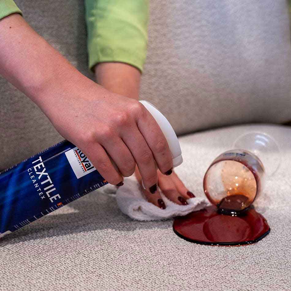 Een vrouw maakt een wijnvlek schoon op een grijze bank