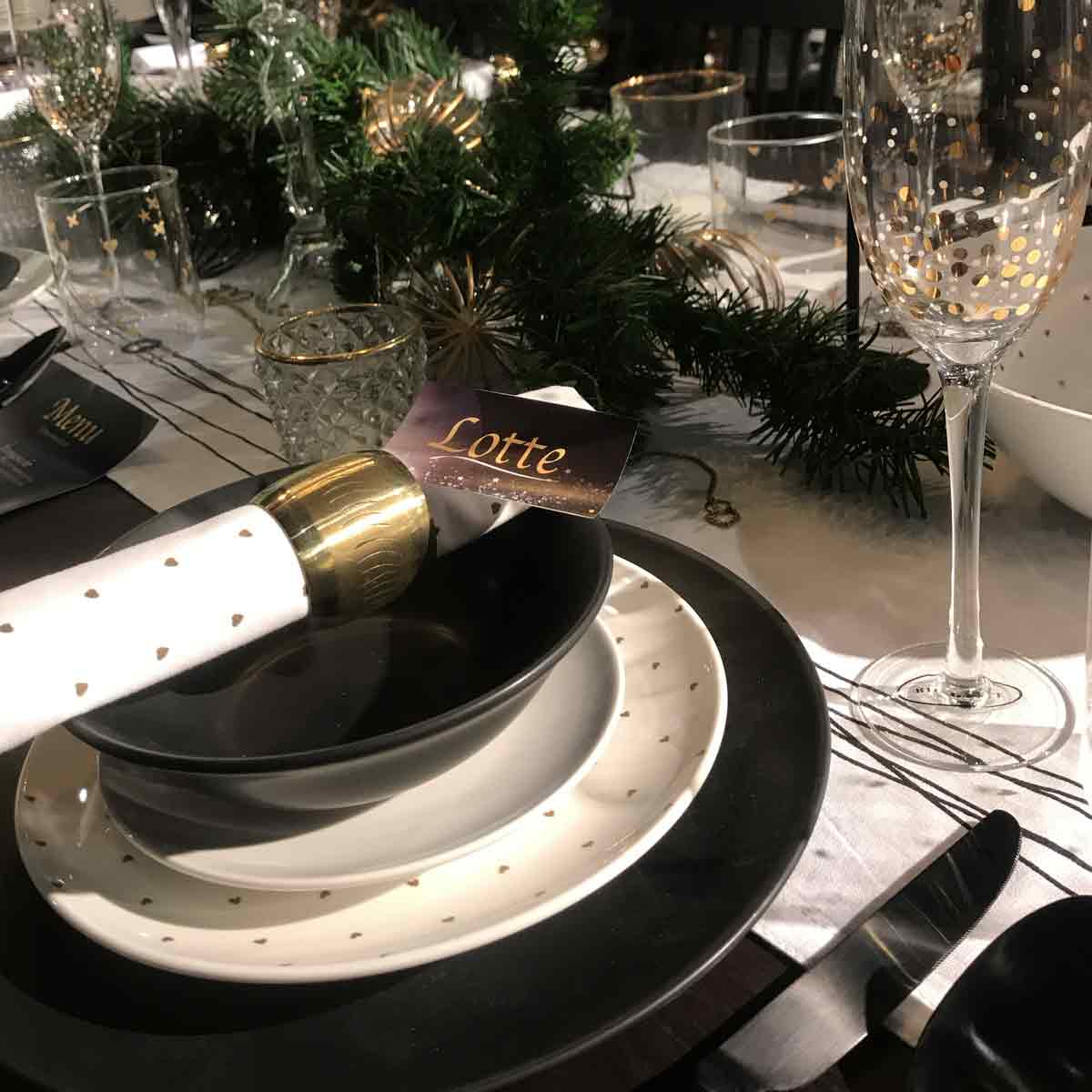Een zwart wit gedekte eettafel met kersttak en gepersonaliseerd naamkaartje
