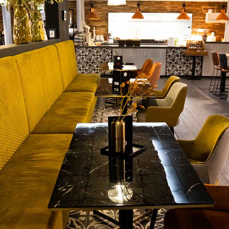 Eethoek in het restaurant met okergele zitbank en zwarte tafeltjes