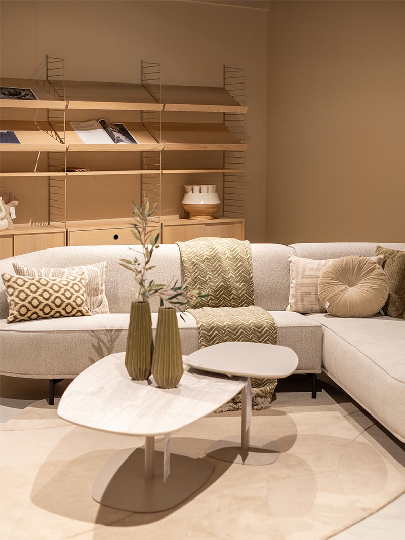 Beige hoekbank met sierkussens en plaid, houten wandkast, salontafels en vazen als Scandinavisch interieur