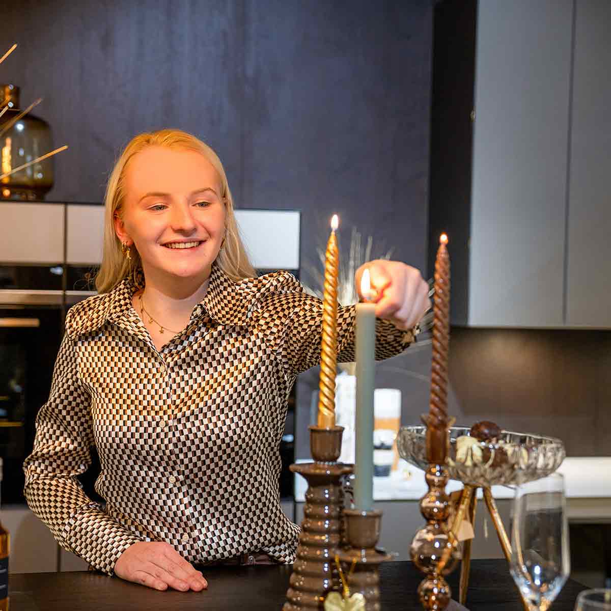 Een blonde vrouw steekt een dinerkaars aan in een bruine kaarsenhouder