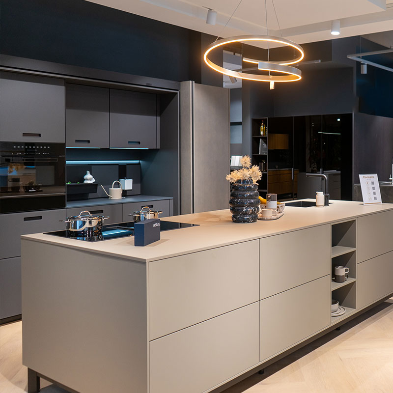 Strakke designkeuken met kookeiland, matzwarte kasten en sfeervolle verlichting in showroomopstelling