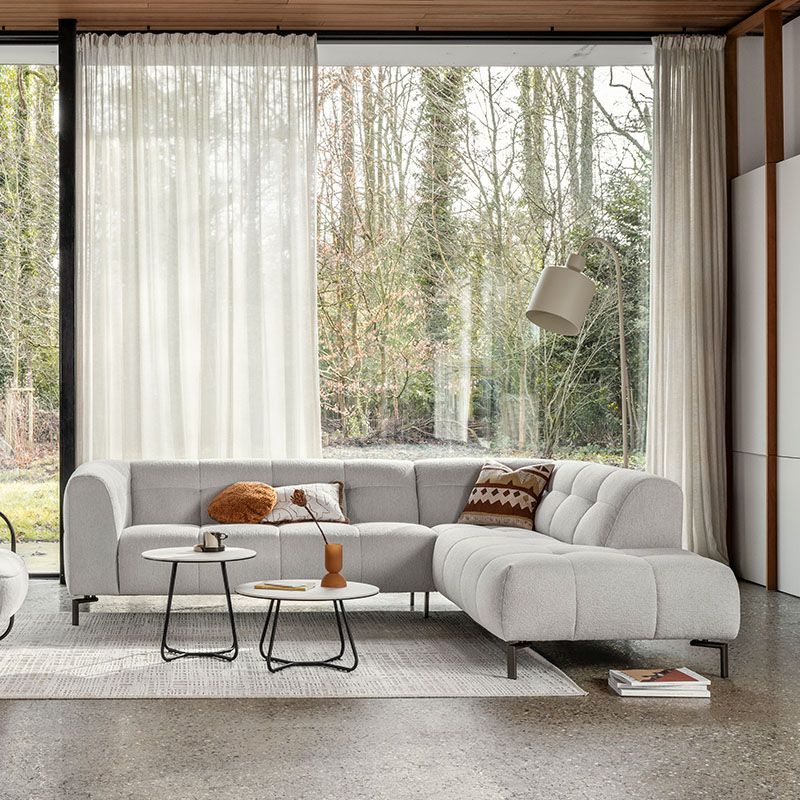 Stijlvolle woonkamer met moderne hoekbank, gekleurde kussens en salontafels op paars vloerkleed