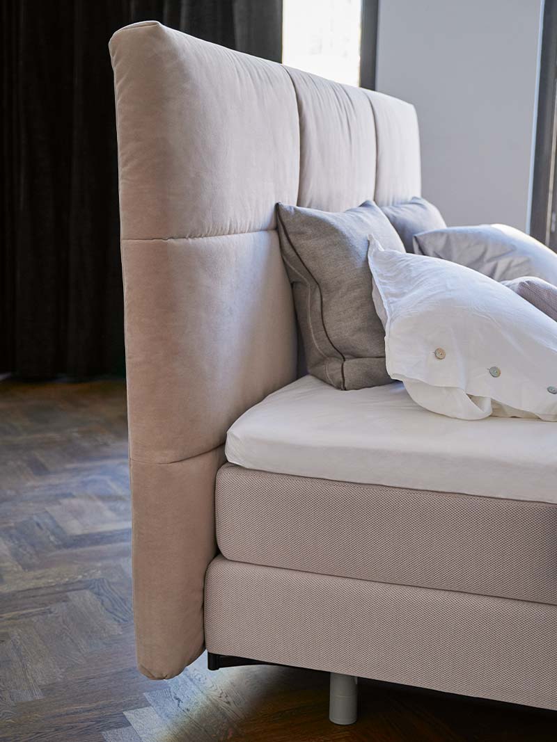 Comfortabel boxspringbed met hoge stoffen hoofdbord en kussens in lichte, serene slaapkamer