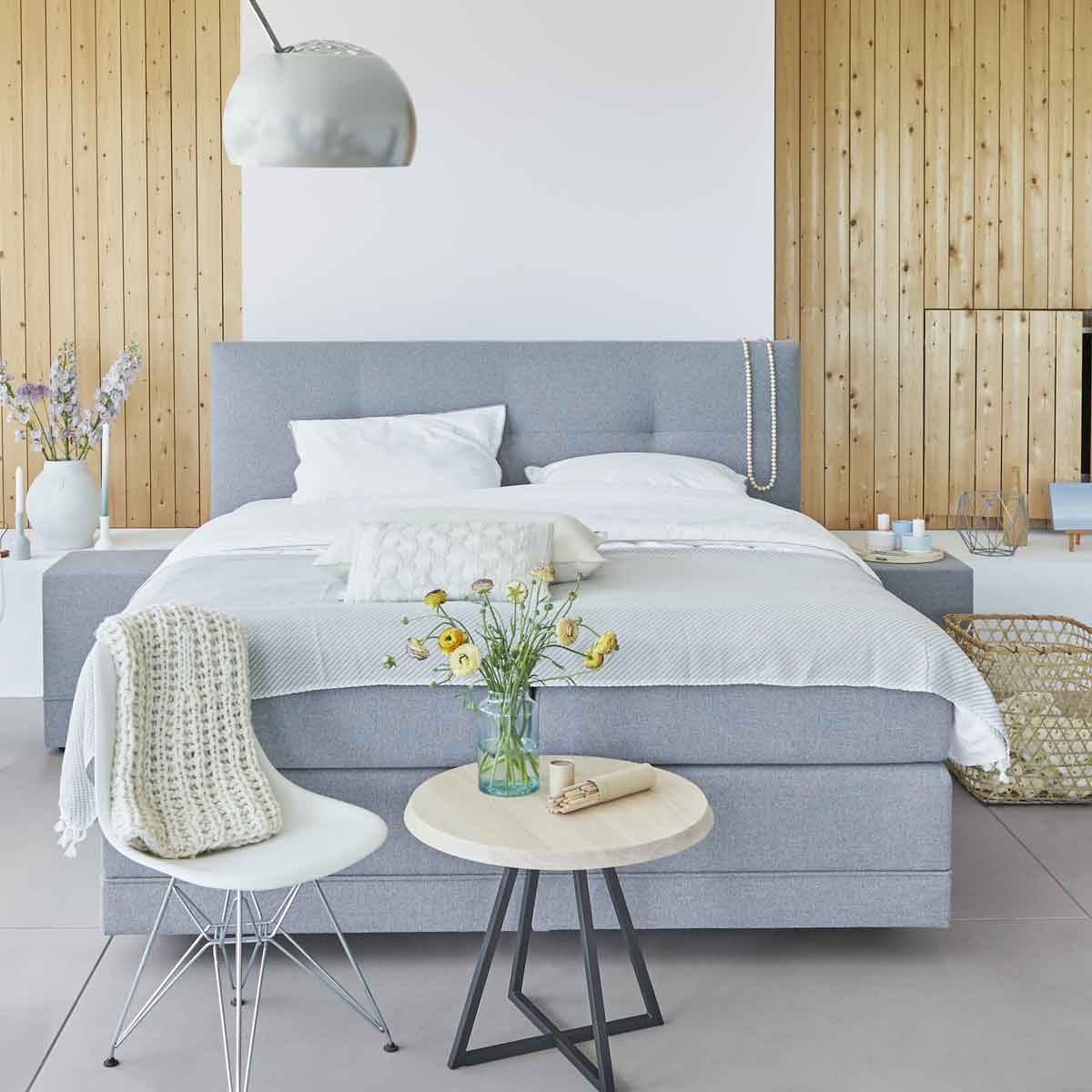 Een slaapkamer met houten achtergrond en een grijze boxspring van Avek met witte lakens