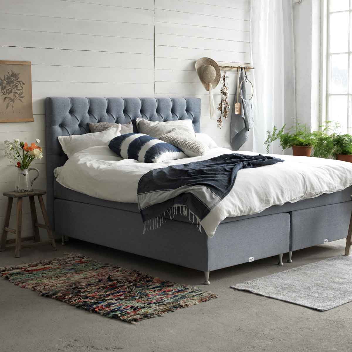 Een grijze boxspring in klassieke rustieke stijl met witte lakens in een slaapkamer