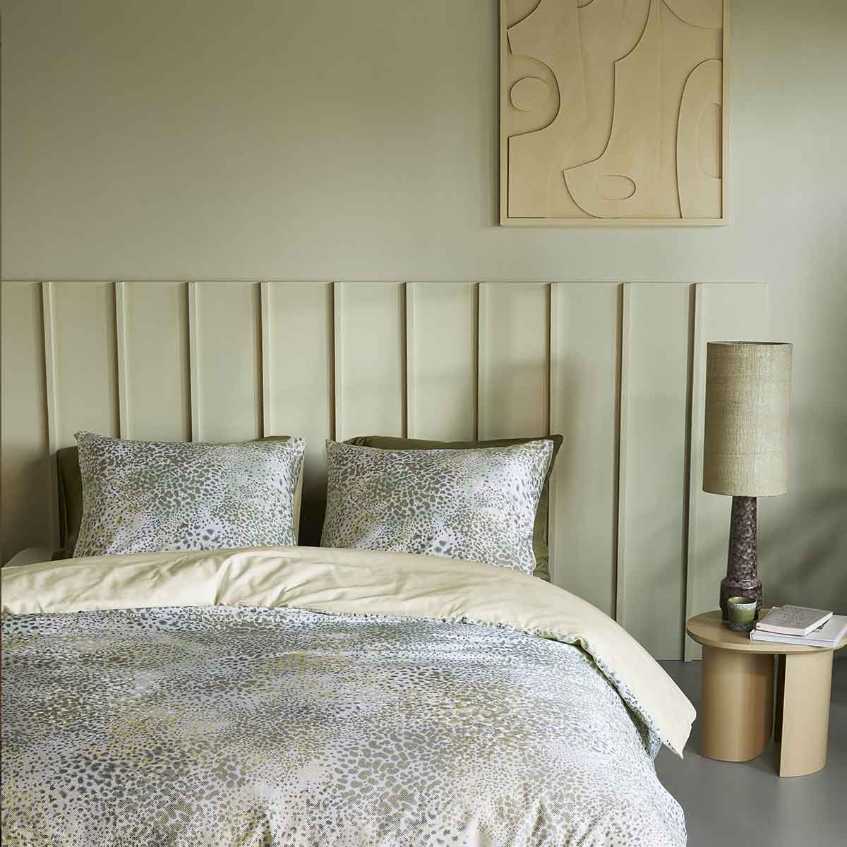 Rustgevende slaapkamer met groen tinten, gestoffeerd hoofdbord, patterned beddengoed en ronde nachttafel met lamp