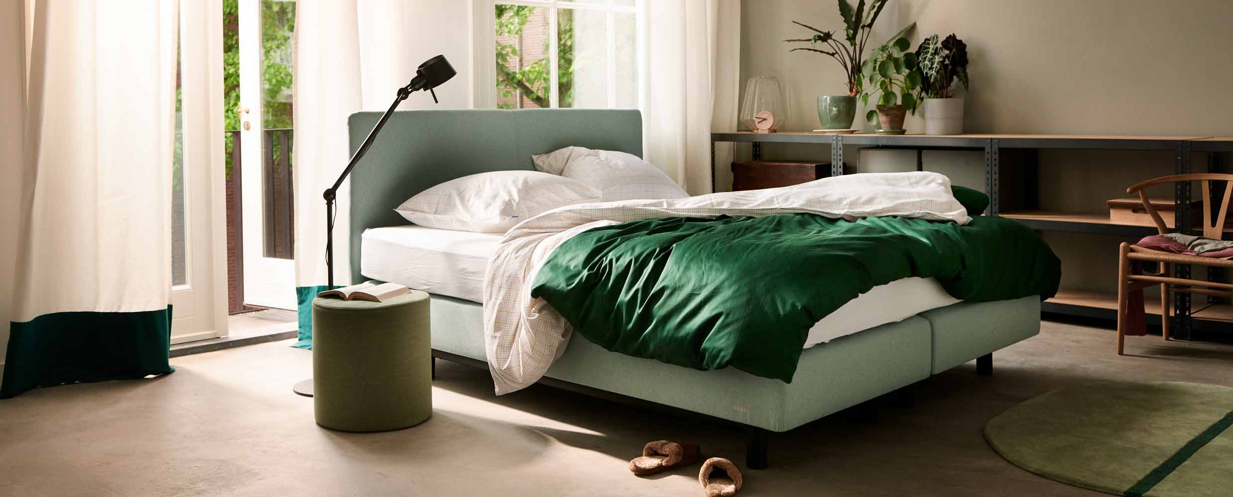 Een groene boxspring van Auping met witte lakens en een groene plaid in een slaapkamer