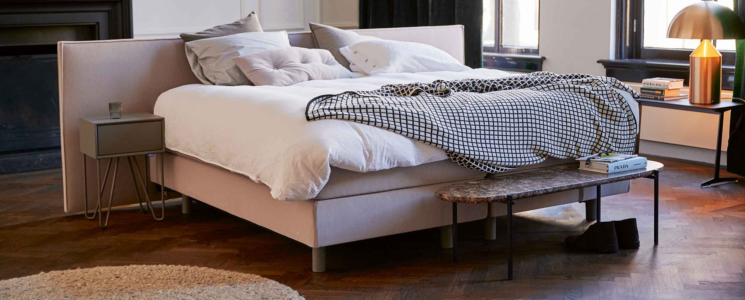 Sfeervolle slaapkamer met licht stoffen bed, witte dekens, marmeren bankje en warm houtvloer