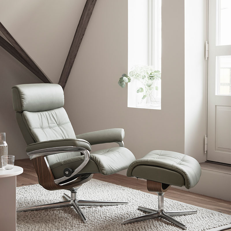 Luxe relaxfauteuil met voetenbank, groene bekleding en houten details bij licht raam