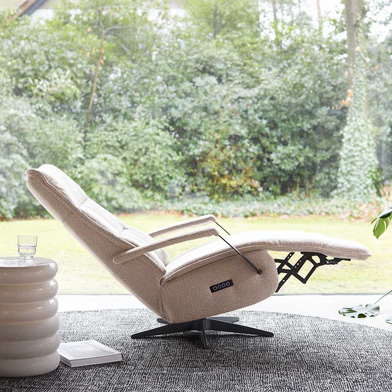 Verstelbare relaxfauteuil in lichte stof met uitklapbare voetensteun bij groot raam en tuinzicht