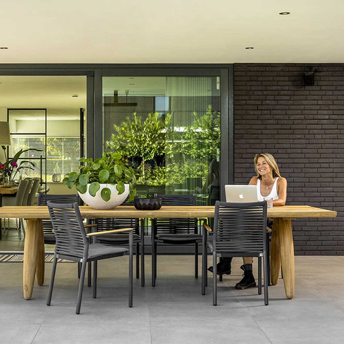 Moderne tuintafel met houten blad, zwarte stoelen en vrouw met laptop op terras