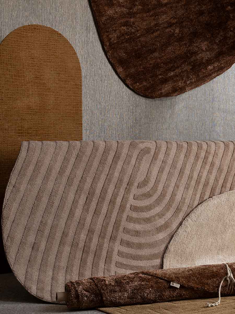 Assortiment moderne vloerkleden in natuurlijke kleuren en organische vormen, met verschillende structuren en patronen, gestyled tegen een grijze wand.