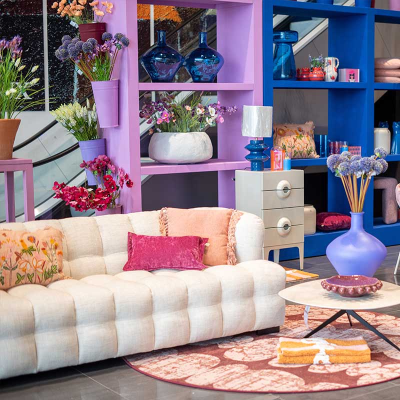 Een trendy hoek in Home Center met witte bank, een kleed, witte bijzettafels en paarse kasten