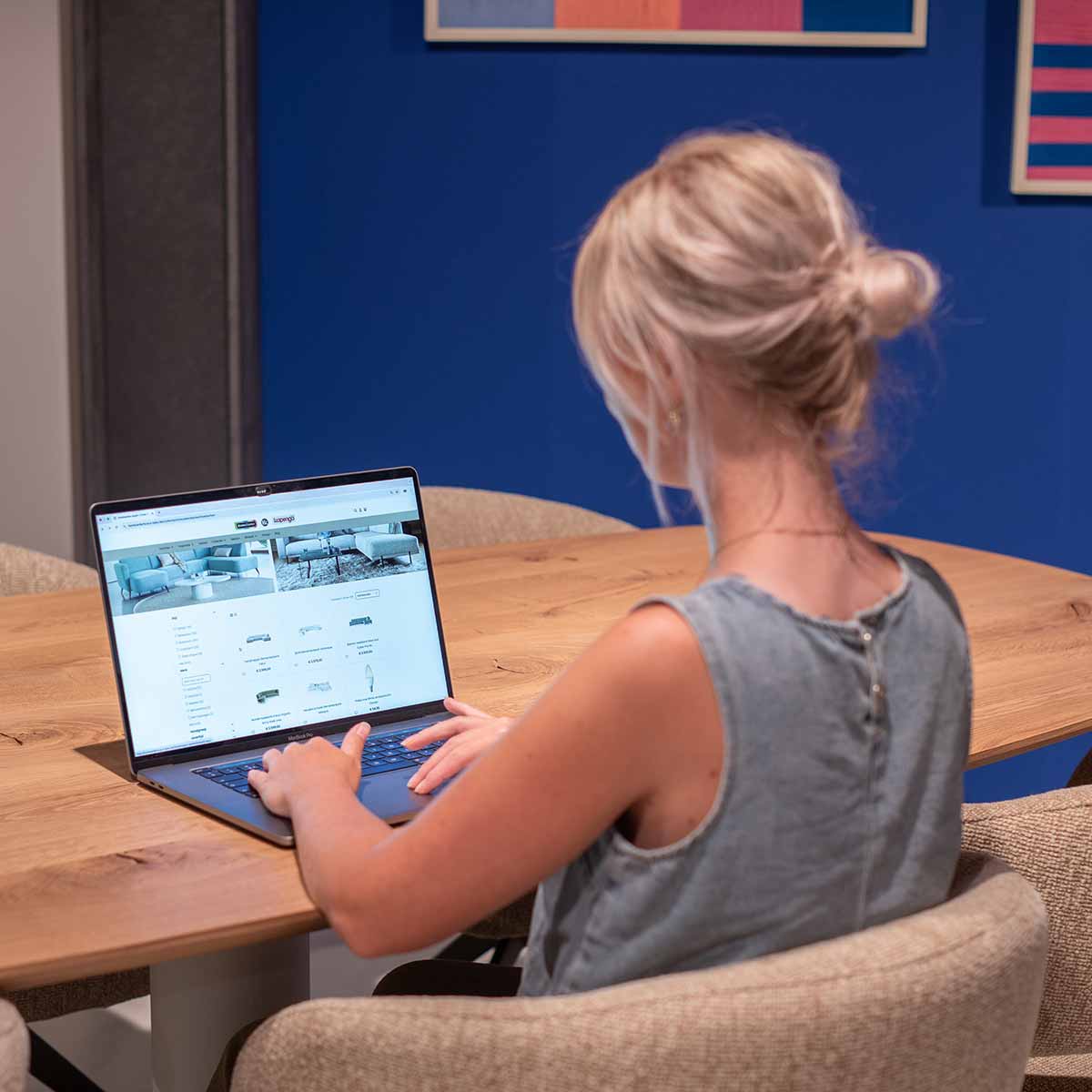 vrouw zit aan een houten eettafel met een laptop
