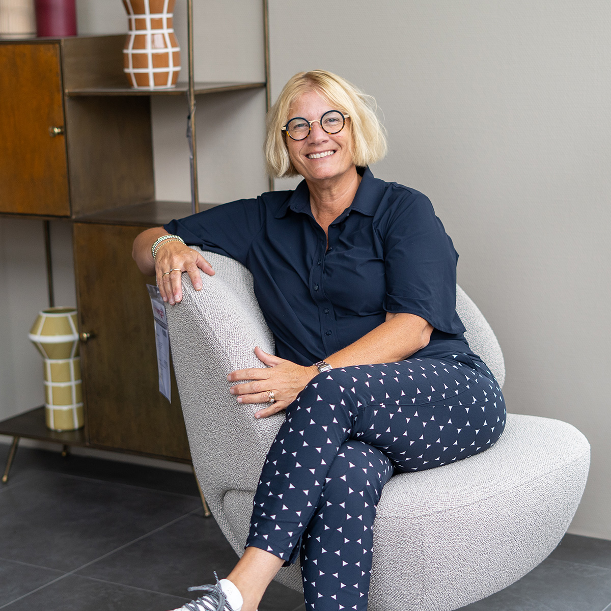 foto van een vrouw in een relaxfauteuil met woonaccessoires en een kast op de achtergrond