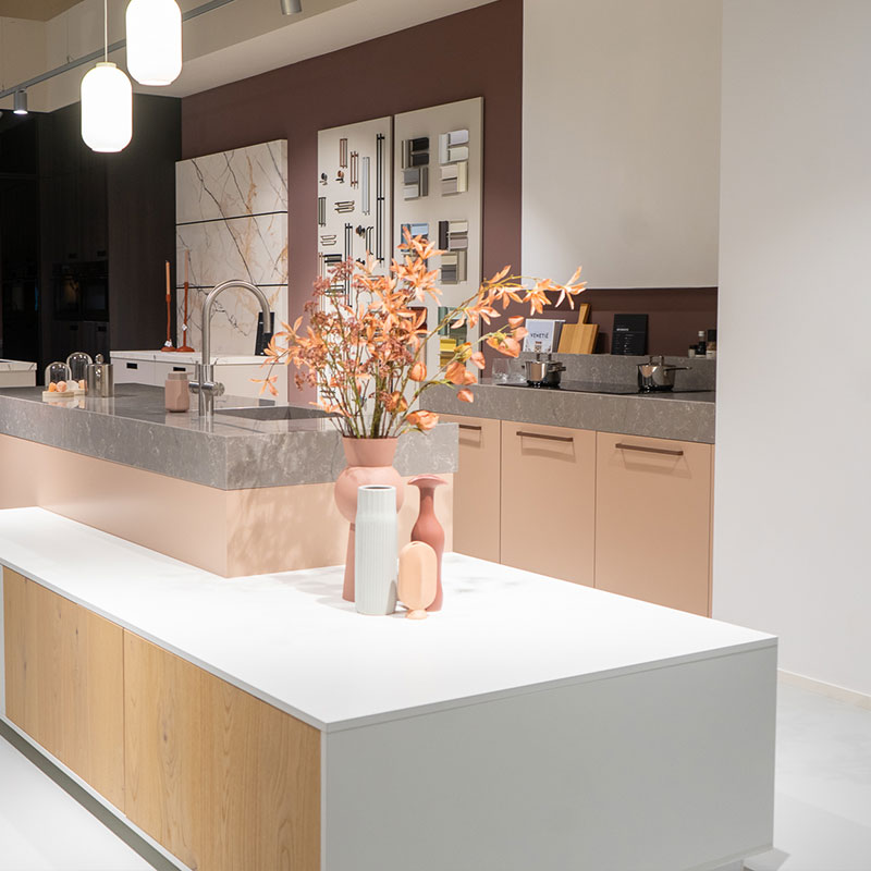 Moderne keuken met roze kasten, grijs werkblad en vaas met oranje takken op kookeiland