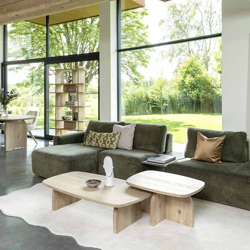 Woonkamer met groene modulaire bank, organische houten salontafels, natuurlijke materialen en grote ramen.