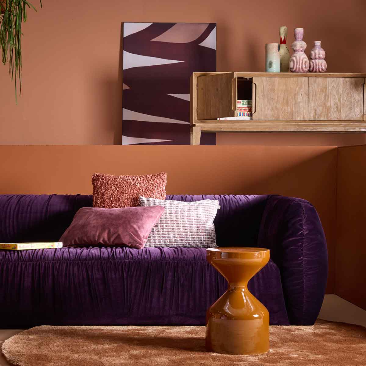 Woontrends 2026 met paarse velvet bank, roze sierkussens, oranje bijzettafel en warme aardetinten in de woonkamer