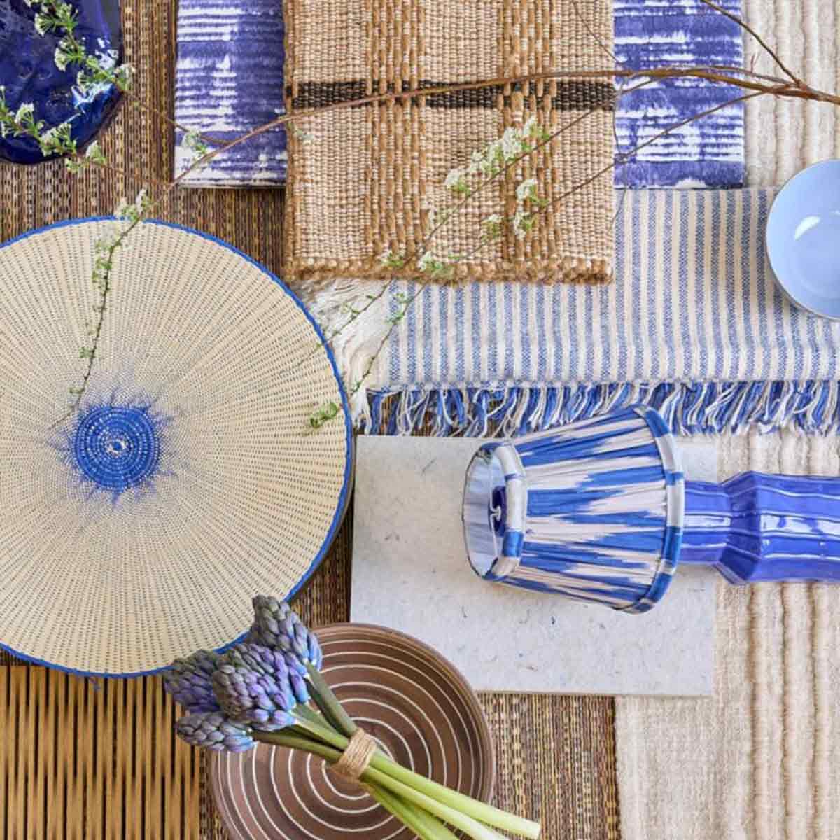 Blauwe en beige woonaccessoires met geweven textiel, keramiek en bloemen op een rustieke ondergrond.