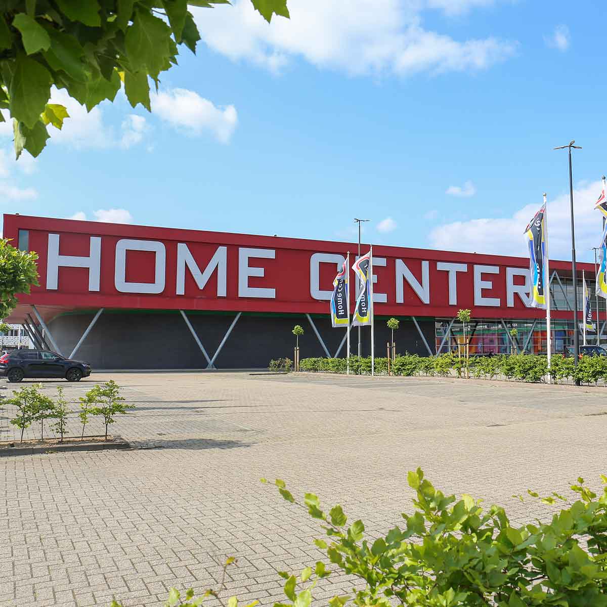 vooraanzicht van Home center woonwinkel met rode gevel en witte letterss, vlaggen en parkeerplaats