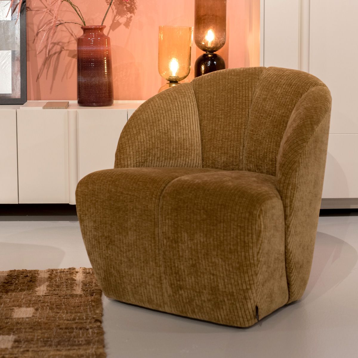 Bruine fauteuil van het merk WOOOD met ronde vormen voor een witte kast met vazen en tafellampen