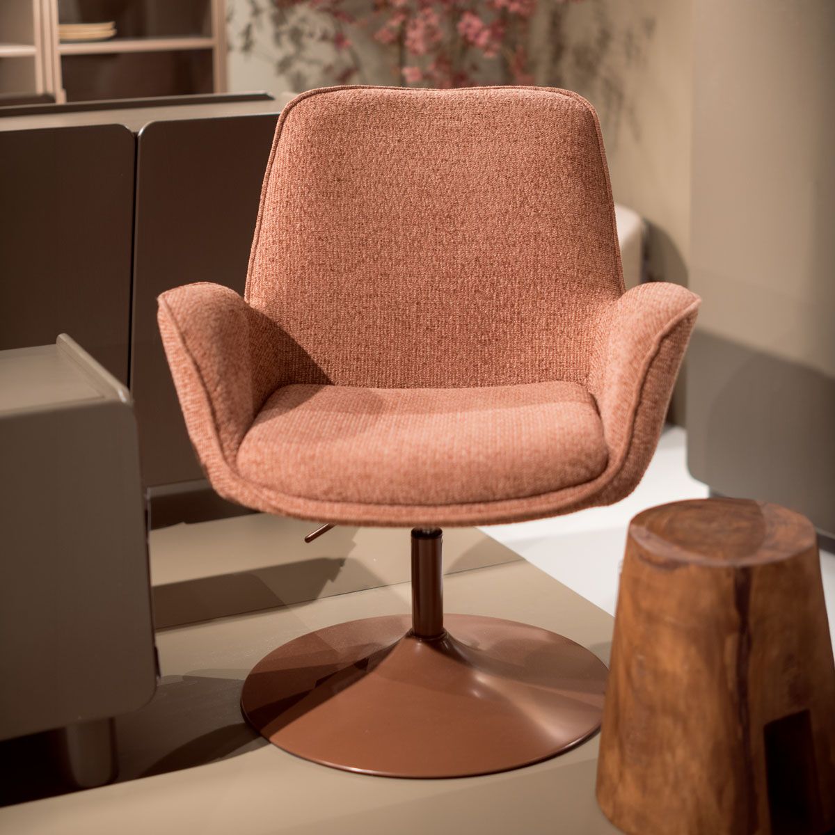 Roze draaifauteuil met armleuningen en ronde metalen voet naast een houten bijzettafel