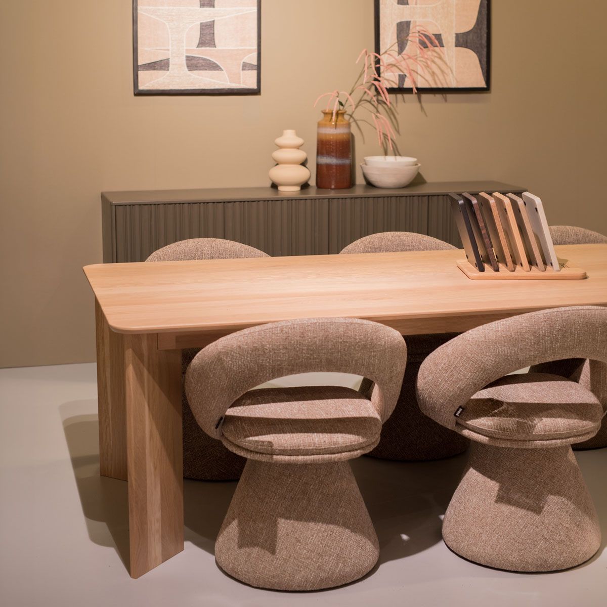 houten eettafel met beige eetkamerstoelen, kleurstalen en kast met vazen op de achtergrond