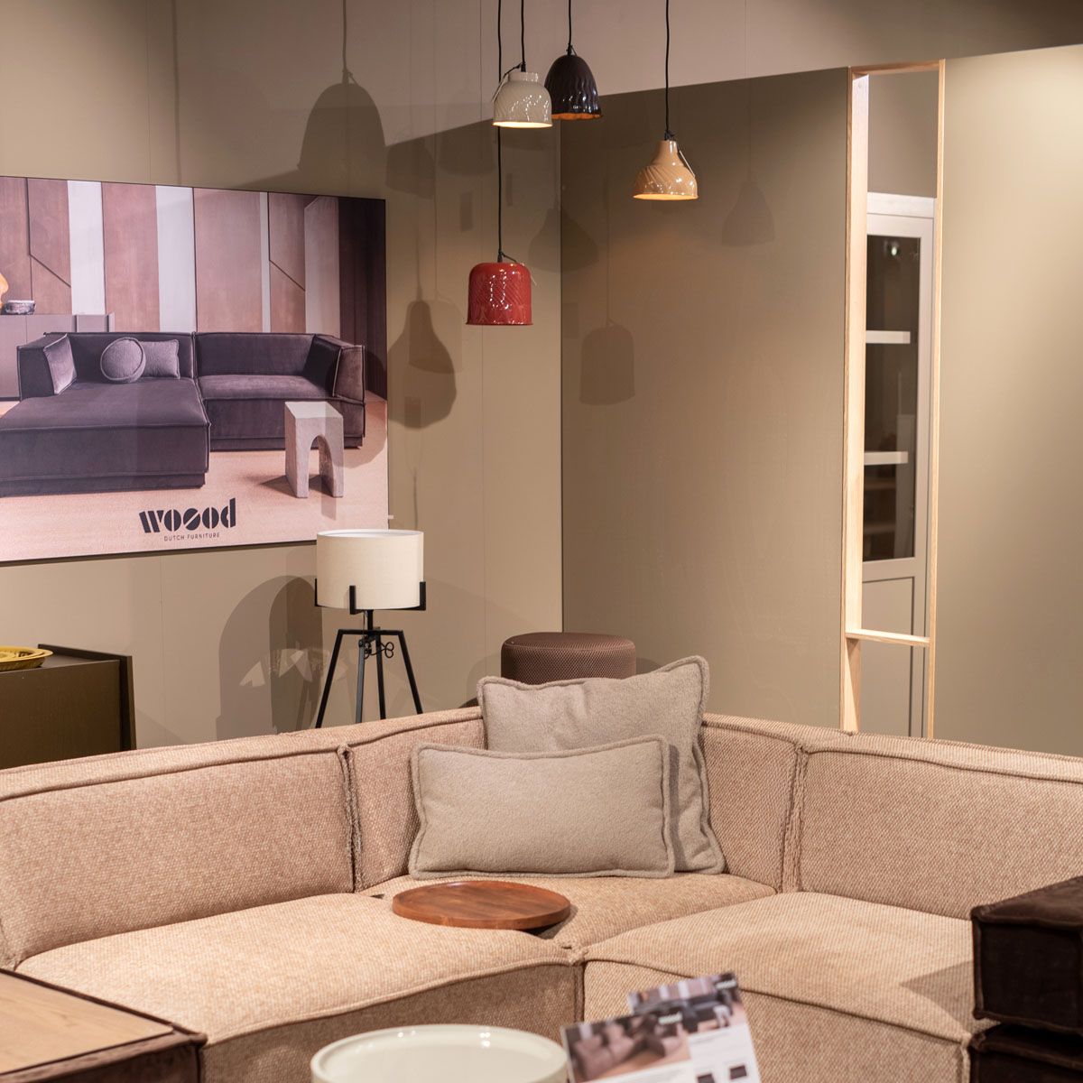 Beige hoekbank met sierkussens in een WOOOD showroom met hanglampen en vloerlamp