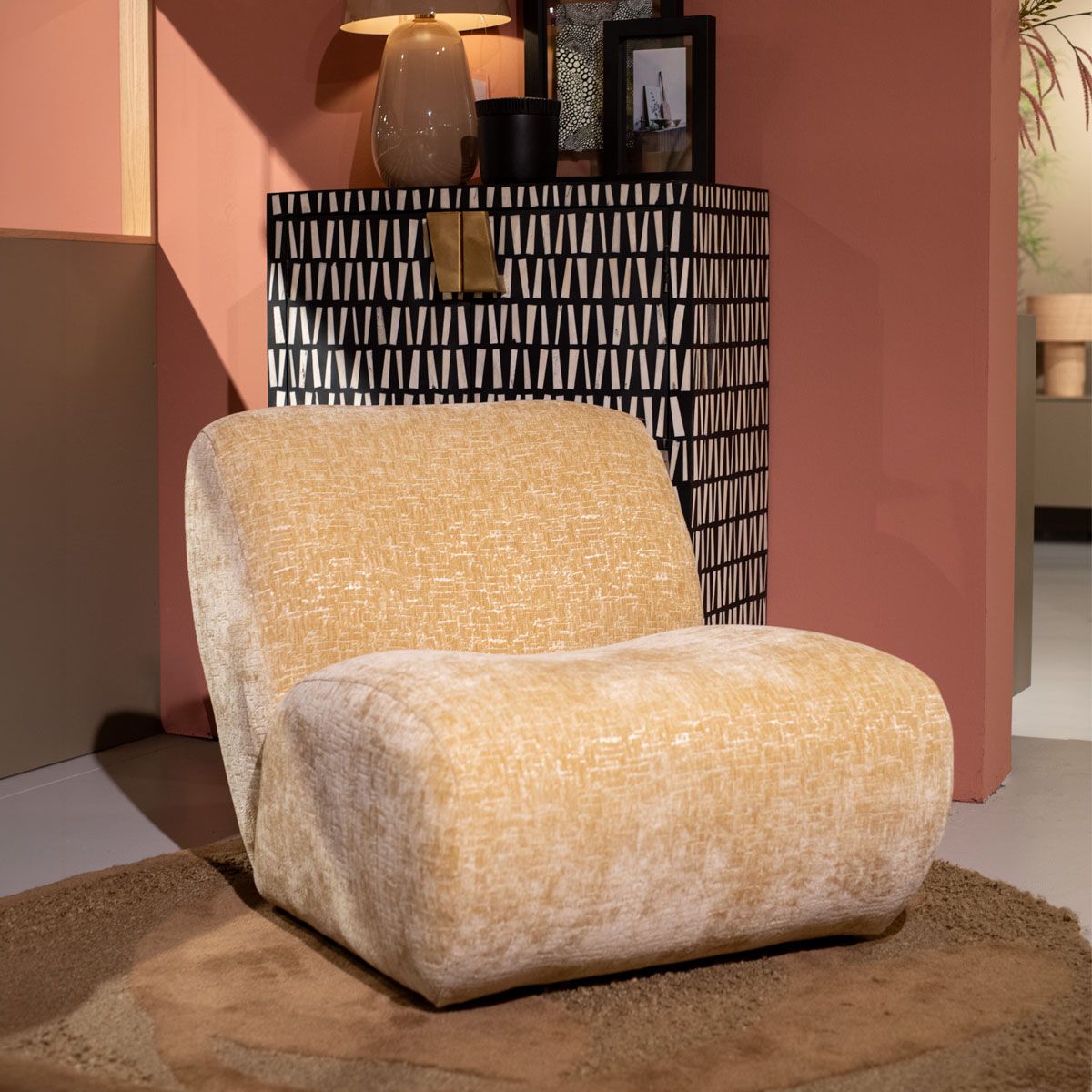 Beige fauteuil met afgeronde vormen voor een zwart-witte kast tegen een roze wand