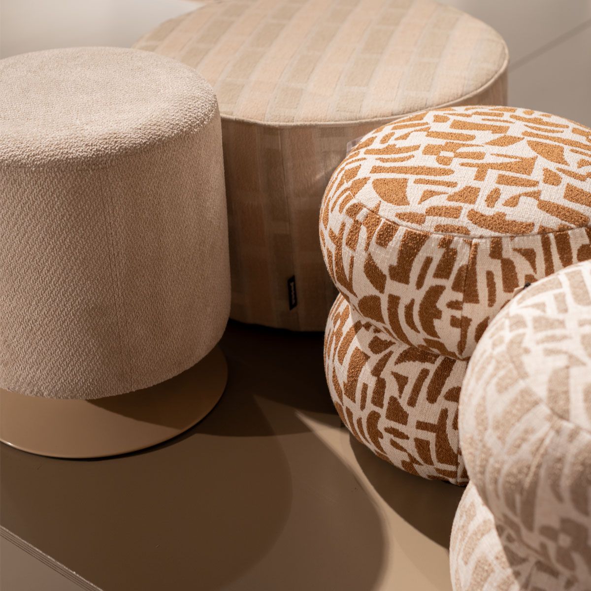 Beige poefs in verschillende vormen en stoffen, waaronder poefs met bruin grafisch patroon