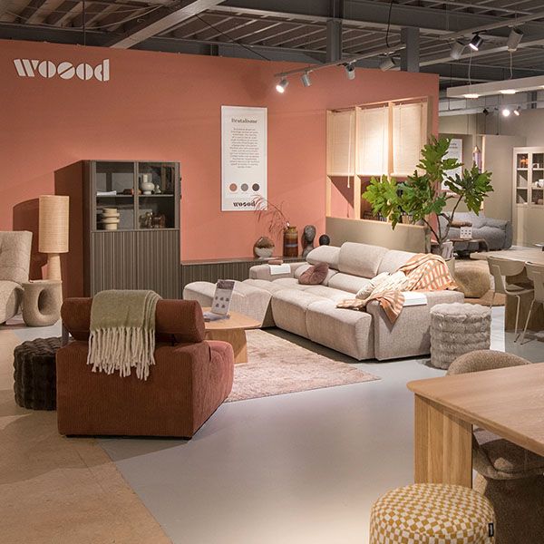 WOOOD showroom met roze wand, beige hoekbank, bruine fauteuil, houten kast, vloerkleed en planten